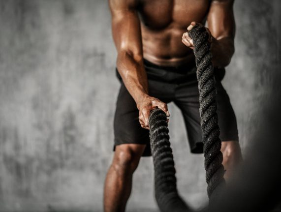 Muscular man working out on the battle ropes in a gym